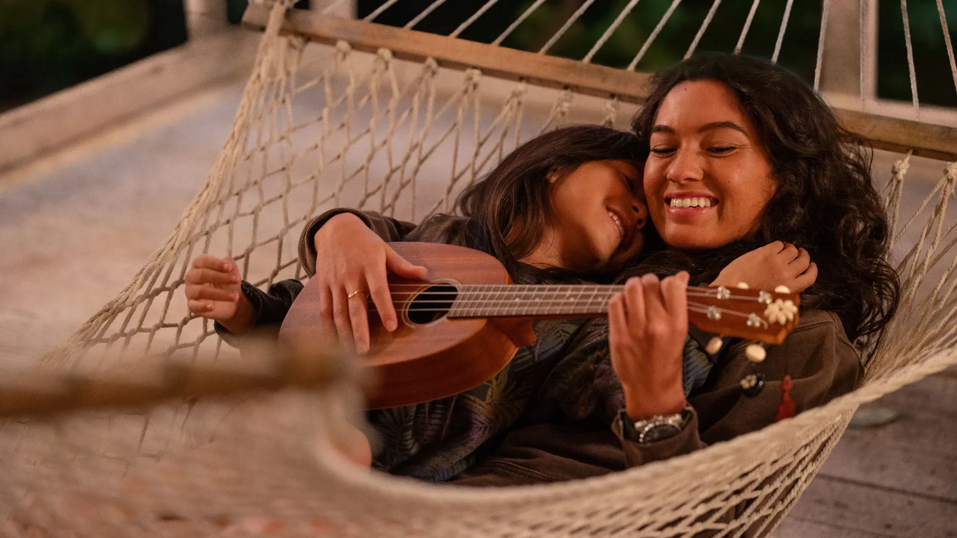 Maia Kealoha and Sydney Agudong smiling, playing a guitar and swinging in a hammock, in the film Lilo & Stitch.